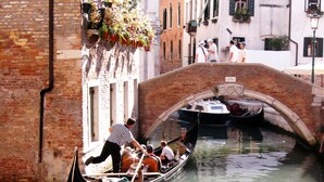 A gondola with passengers and a gondolier navigating under a bridge in a canal. - Charming, views Of Canals, Gondolas, Church Of The Miracoli (Venezia)