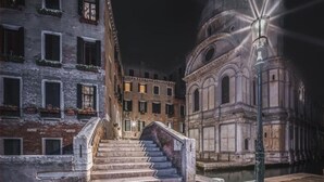 A nighttime view of a historic building with a staircase leading to a gated entrance, surrounded by other buildings with visible windows and balconies. - Charming, views Of Canals, Gondolas, Church Of The Miracoli (Venezia)
