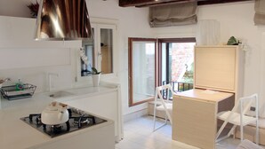 A compact kitchen with white cabinetry, a gas stove, and a hanging light fixture. - Charming, views Of Canals, Gondolas, Church Of The Miracoli (Venezia)