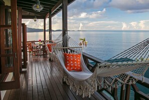 A wooden deck with a hammock, chairs, and a table with a flower vase.