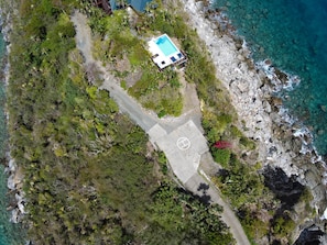 Una vista aerea di una proprietà costiera con piscina, vialetto lastricato e terreno roccioso.