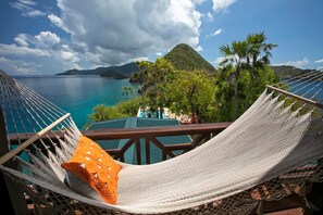 A hammock chair with a cushion, overlooking a turquoise sea and a mountainous landscape.