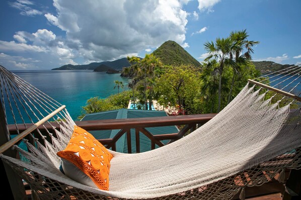 A hammock chair with a cushion, overlooking a turquoise sea and a mountainous landscape. - The Treehouse at Steele Point (West End)