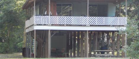 A two-story wooden house with a balcony, surrounded by trees.