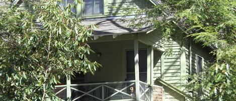 A green wooden cabin with a stone foundation, a porch, and a gravel path leading to the entrance.