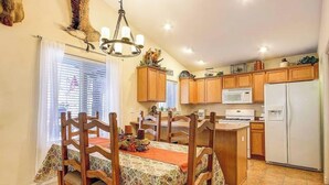 A dining area with wooden chairs and a table, a kitchen with wooden cabinets and appliances, and a chandelier.