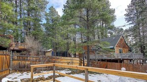 A wooden deck with a wooden railing, surrounded by snow-covered ground and trees.