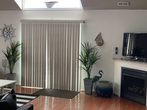 A living room with a large window, a television, a fireplace, and two potted plants.