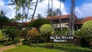 Ein Resort mit einem Steinschild, das "NiHi Kai Villas Resort" zeigt, umgeben von üppiger Vegetation und hohen Palmen.