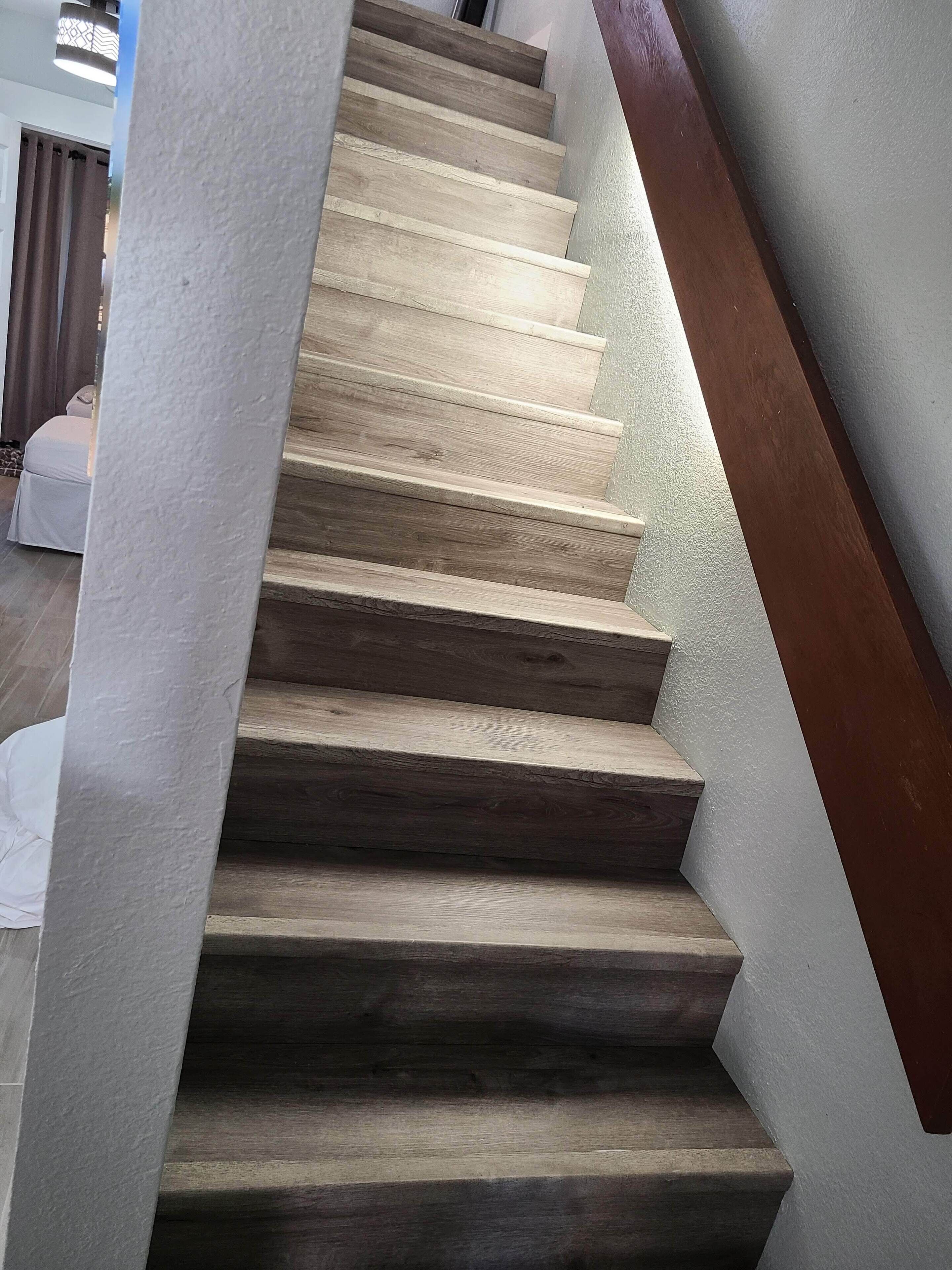 A wooden staircase with a white wall and a brown handrail.