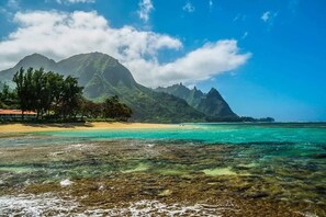 Ein Strand mit klarem türkisblauem Wasser, sandigem Ufer und einem Berg im Hintergrund.