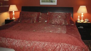 A neatly made bed with a red bedspread and matching pillows, flanked by two bedside tables with lamps and a framed picture on the wall above. - Right in the middle of the action Safe comfort  (Miraflores)