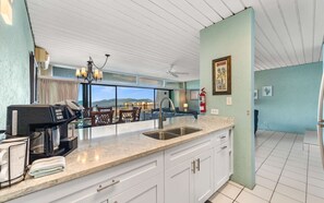 A kitchen with a coffee machine, a sink, and a view of the ocean.