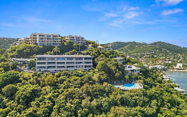 A multi-story hotel with a pool, surrounded by lush greenery and hills.