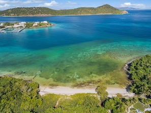 A coastal area with clear waters, a beach, and a small island with buildings.