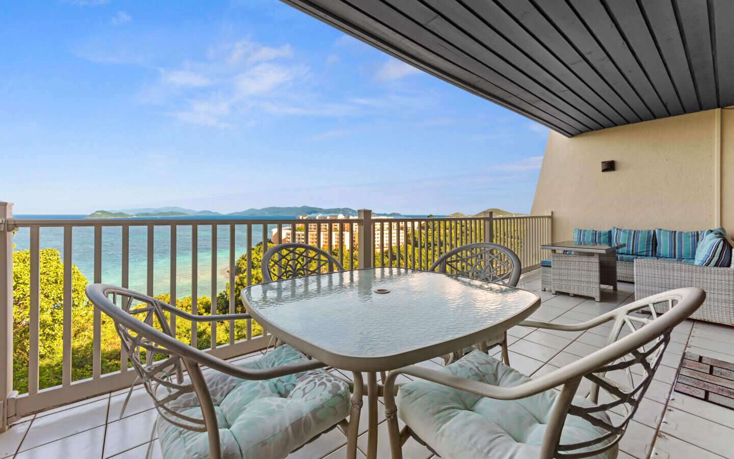 A balcony with a table and chairs, a sofa, and a view of the sea.