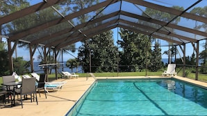 Une piscine à eau claire, dotée d’un espace abrité, de chaises longues et offrant une vue sur l’océan.