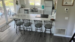 Een moderne keuken met een marmeren eiland, vier barkrukken, een koelkast en een raam met uitzicht op een balkon.