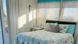 Een slaapkamer met een bed, nachtkastje, vloerkleed en raam met gordijnen.