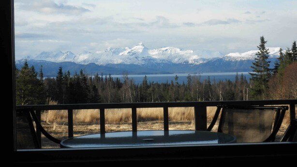 A view from a window with a metal railing, overlooking a lake and snow-capped mountains. - You have to get out-of-town to see the wildlife (Homer)