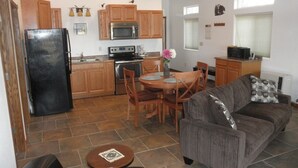 A compact kitchen with wooden cabinets, a refrigerator, microwave, and stove. There's a dining area with a table and chairs, and a living room with a sofa. - You have to get out-of-town to see the wildlife (Homer)