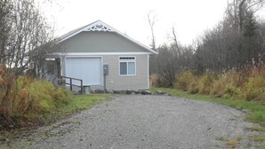 A single-story building with a garage, surrounded by gravel and vegetation. - You have to get out-of-town to see the wildlife (Homer)