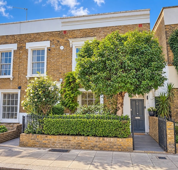 A two-story brick house with a front garden, a black door, and a white window frame.