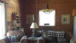 Ein gemütliches Blockhaus-Interieur mit Holzboden, Ledersofas, einem Holztisch und einer Chandelüstere.