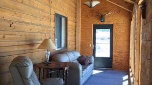 Ein Holzblockhaus-Innenraum mit Sofa, Sesseln und Deckenventilator.