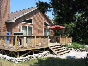 A wooden deck with a stone wall, outdoor furniture, and a red umbrella.