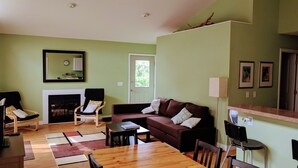 A living room with a wooden table, a brown sofa, a black chair, and a fireplace. - Cedar Cottage - Kelleys Island (Lake Erie) Vacation Retreat (Kelleys Island)