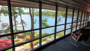A covered deck with large windows overlooking a lake, a dock, and a statue. - "One-of-a-kind" Lake Martin Property With Large Boat Ramp, Boathouse & Pier (Dadeville)