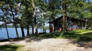 A cabin by a lake with a gravel path leading to it, surrounded by trees. - "One-of-a-kind" Lake Martin Property With Large Boat Ramp, Boathouse & Pier (Dadeville)