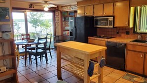 A kitchen with wooden cabinets, a microwave, a refrigerator, and a dining area with chairs and a table. - "One-of-a-kind" Lake Martin Property With Large Boat Ramp, Boathouse & Pier (Dadeville)