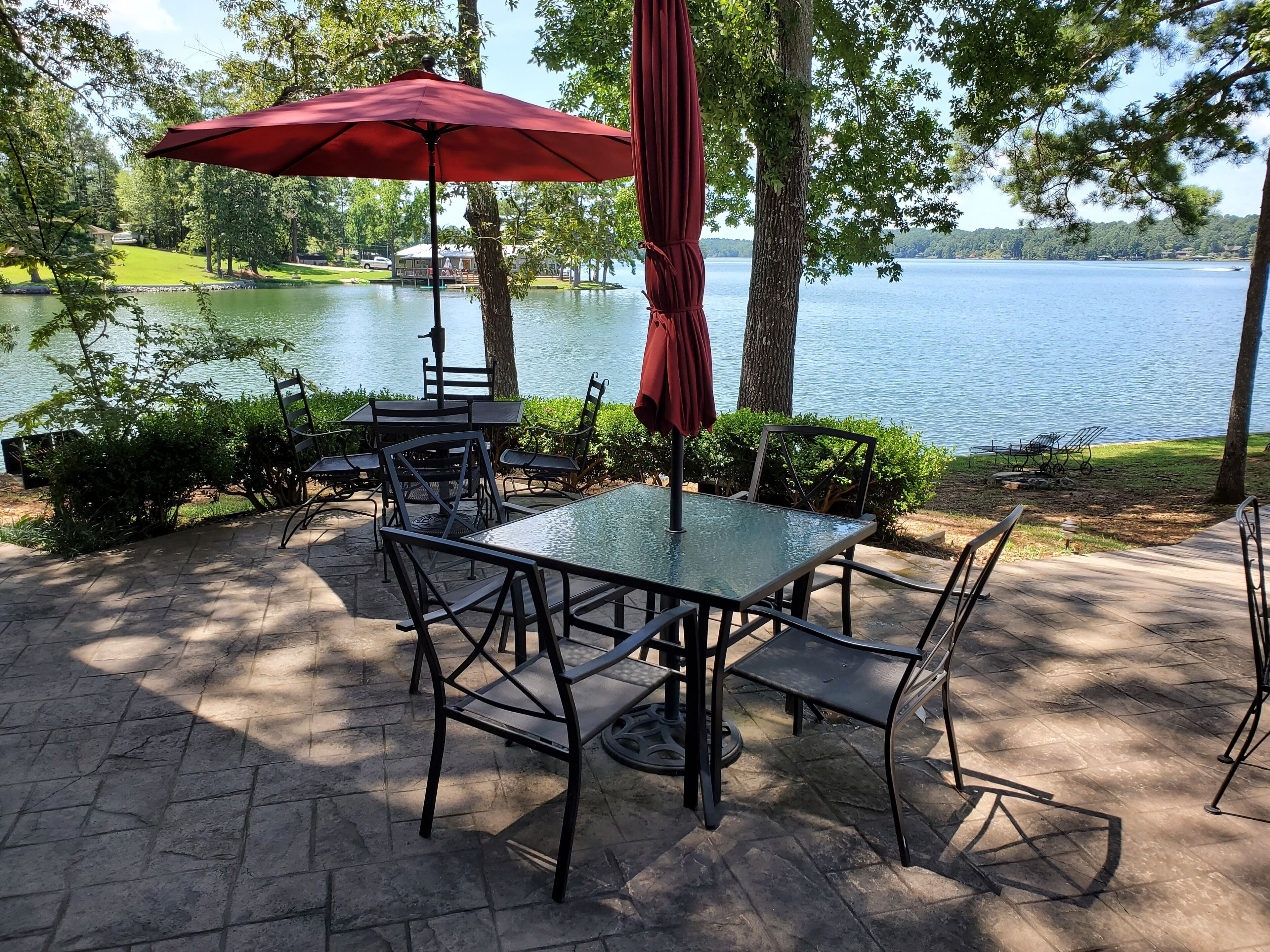 Un patio al aire libre con una mesa y sillas de vidrio, un paraguas rojo y vistas a un lago.