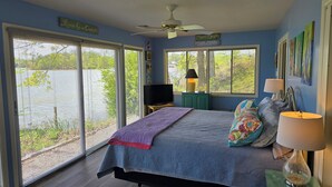 A bedroom with a bed, two bedside lamps, a ceiling fan, a TV on a stand, and large windows with blinds. - "One-of-a-kind" Lake Martin Property With Large Boat Ramp, Boathouse & Pier (Dadeville)