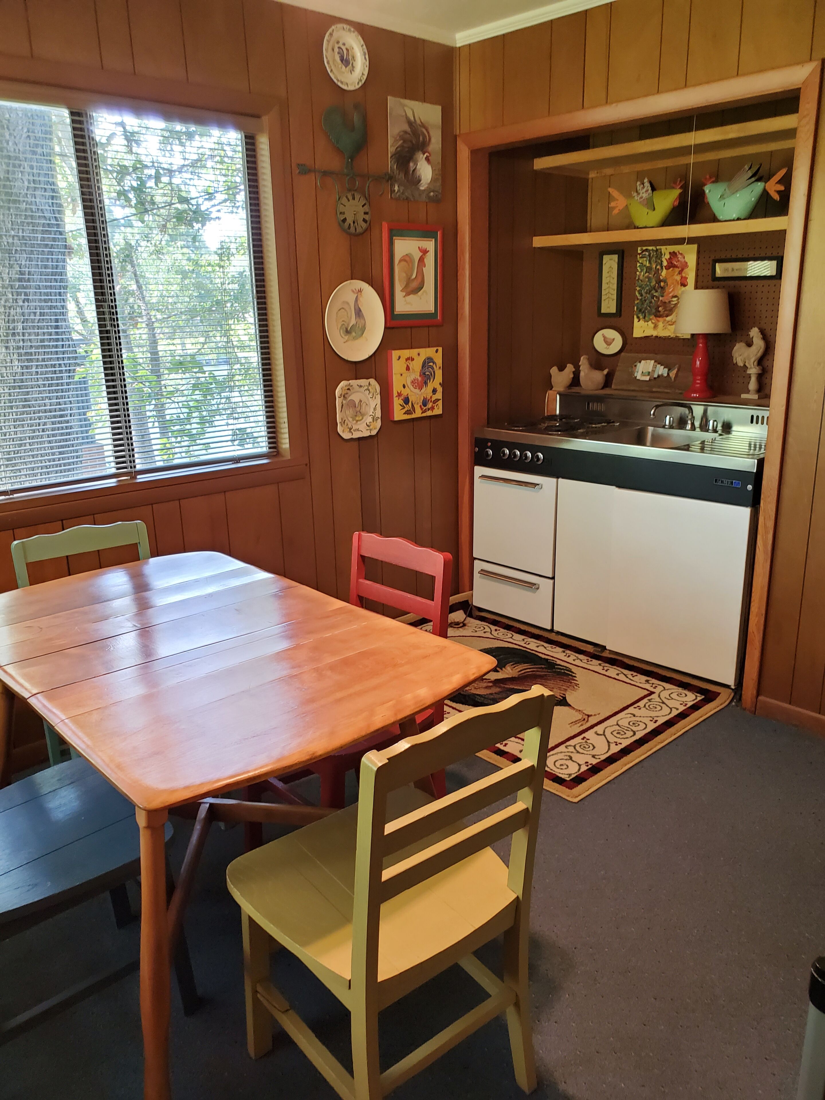 Habitación con paneles de madera, una mesa de comedor, sillas, una zona de cocina con estufa y diversas decoraciones en las paredes.