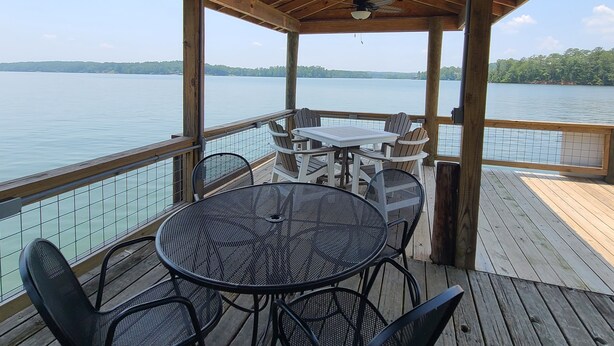 A covered outdoor deck with a table and chairs, overlooking a body of water. - "One-of-a-kind" Lake Martin Property With Large Boat Ramp, Boathouse & Pier (Dadeville)