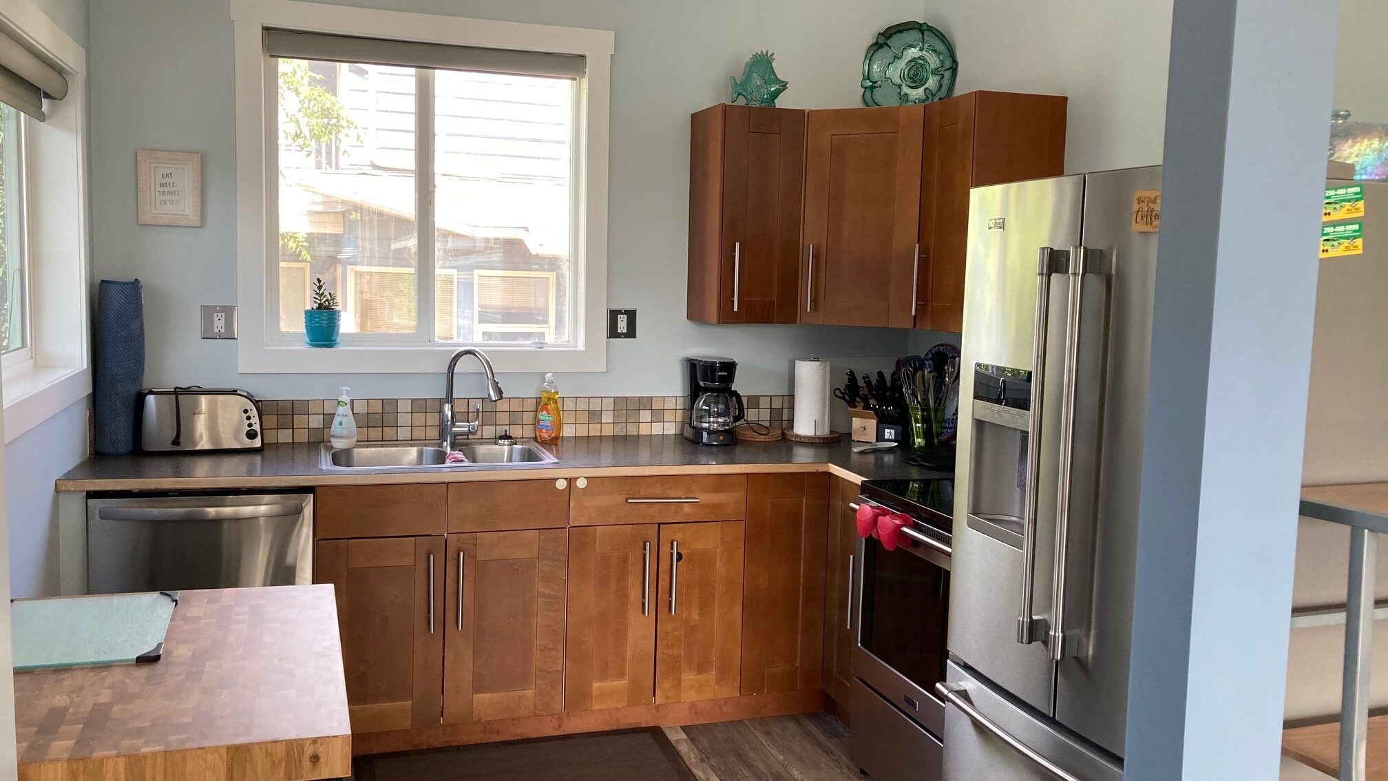 Een moderne keuken met houten kastjes, roestvrijstalen apparatuur en een raam dat natuurlijk licht biedt.
