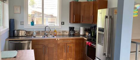 Een moderne keuken met houten kastjes, roestvrijstalen apparatuur en een raam dat natuurlijk licht biedt.