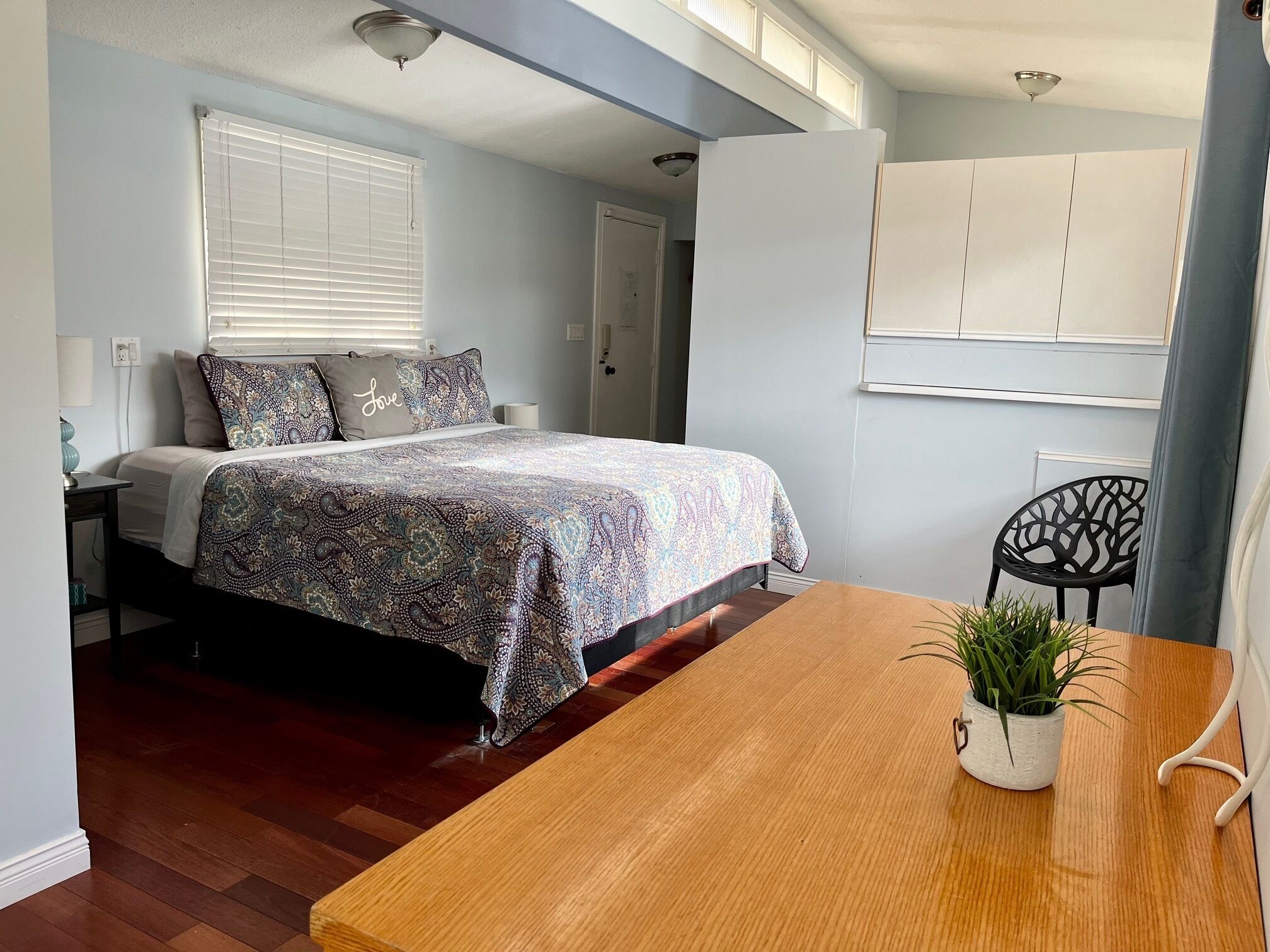 A bedroom with a bed, bedside table, and a wooden table with a plant.