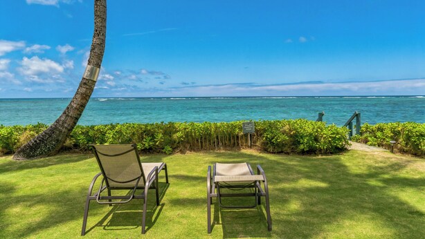 A view of a beach with two lounge chairs facing the ocean, a palm tree, and a sign indicating a private area. - Spacious one bedroom condo on a white sandy beach! (Hauula)