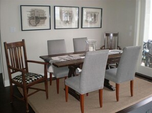 Un comedor con una mesa de madera, sillas tapizadas en gris y tres obras de arte enmarcadas en la pared.