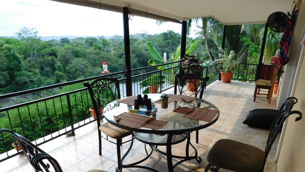 A balcony with a glass table, chairs, and potted plants. - Wish Willy Getaway Cabana  (Santa Elena)