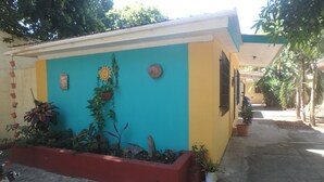 A small, colorful building with a blue and yellow facade, surrounded by potted plants and a concrete pathway. - Wish Willy Getaway Cabana  (Santa Elena)