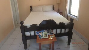 A bedroom with a bed, a bedside table with a remote control, a clock, and a window. - Wish Willy Getaway Cabana  (Santa Elena)
