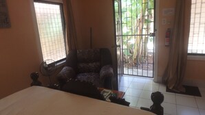 A room with a bed, a patterned armchair, a standing fan, a door leading outside, and a fire extinguisher on the wall. - Wish Willy Getaway Cabana  (Santa Elena)