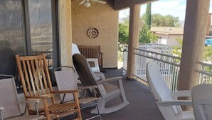 A covered outdoor seating area with a mix of wooden and white plastic chairs, a ceiling fan, and a decorative wall piece. - 5 Minutes From The Lake! Million Dollar Views! (Page)