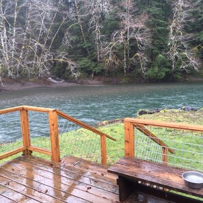 A wooden deck with a metal railing overlooking a river, surrounded by trees. - solduc river cabin near forks  (port angeles)