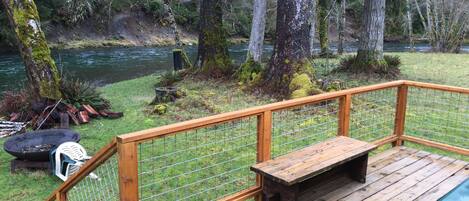 A wooden deck with a bench and a table, overlooking a river and forested area.